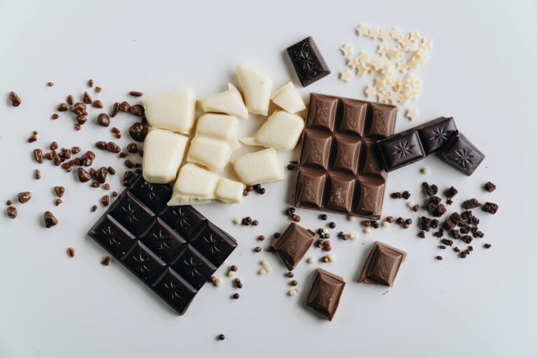 An artistic flat lay of assorted dark, white, and milk chocolate bars with chocolate crumbles.